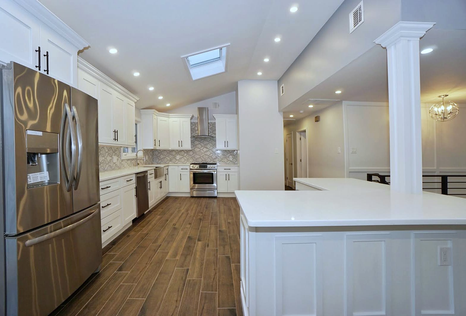 Remodeled kitchen with white cabinets, stainless appliances, wood-look tile floor, column